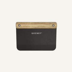 A Gozney kitchen scraper dough cutter with a matte black metal body and a natural light wood handle, shown against a solid off-white background.