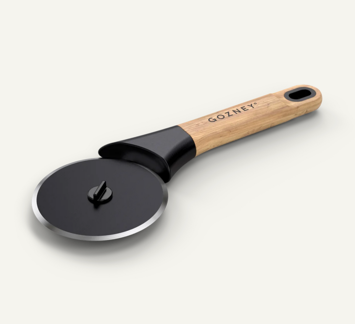 A Gozney pizza cutter with a black metal wheel, black guard, and a light wood handle, shown on a clean off-white background.