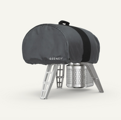 A dark gray Gozney tent cover with a black strap, draped over a silver aluminum camping stove, on a clean off-white background.