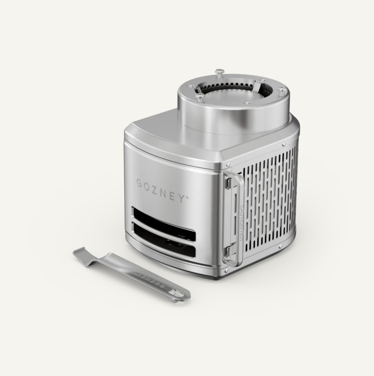 A silver metallic portable stove by GOZNEY with a matching metal tool placed in front, shown on a clean off-white background.